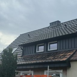 Ciesielstwo-Dekarstwo SŁAW-DACH - Dom z dachem pokrytym brązową dachówką ceramiczną, z nową, ciemną obróbką blacharską i orynnowaniem. Widoczne okna dachowe i fragment rusztowania.