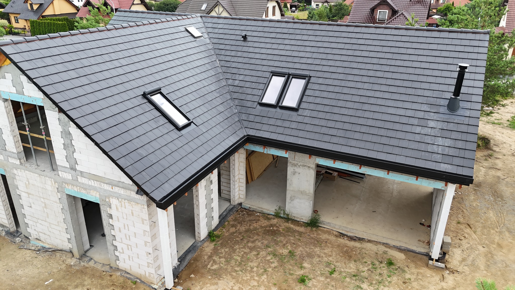 Nowy, grafitowy dach z dachówki ceramicznej z oknami dachowymi na surowym budynku w trakcie budowy, widok z góry.