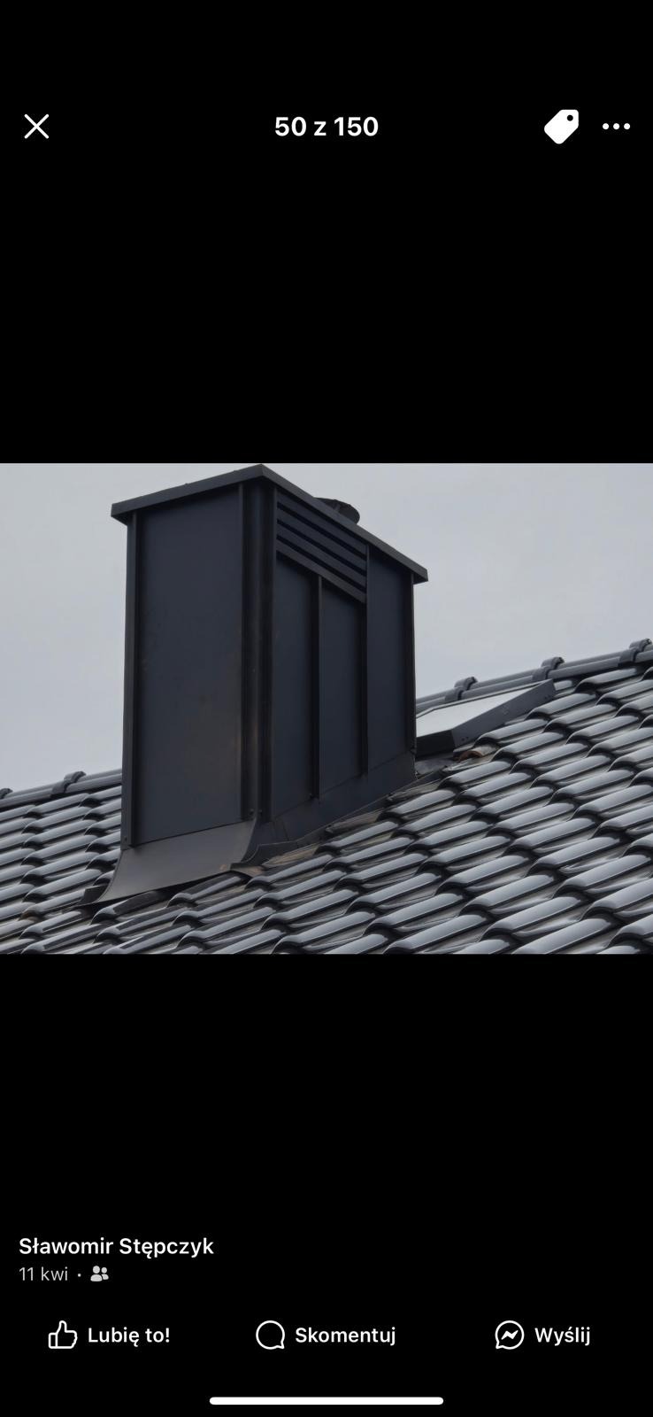 Czarny komin wentylacyjny na dachu pokrytym ciemną dachówką ceramiczną. Nowoczesna obróbka blacharska komina. Widok z dołu na tle pochmurnego nieba.