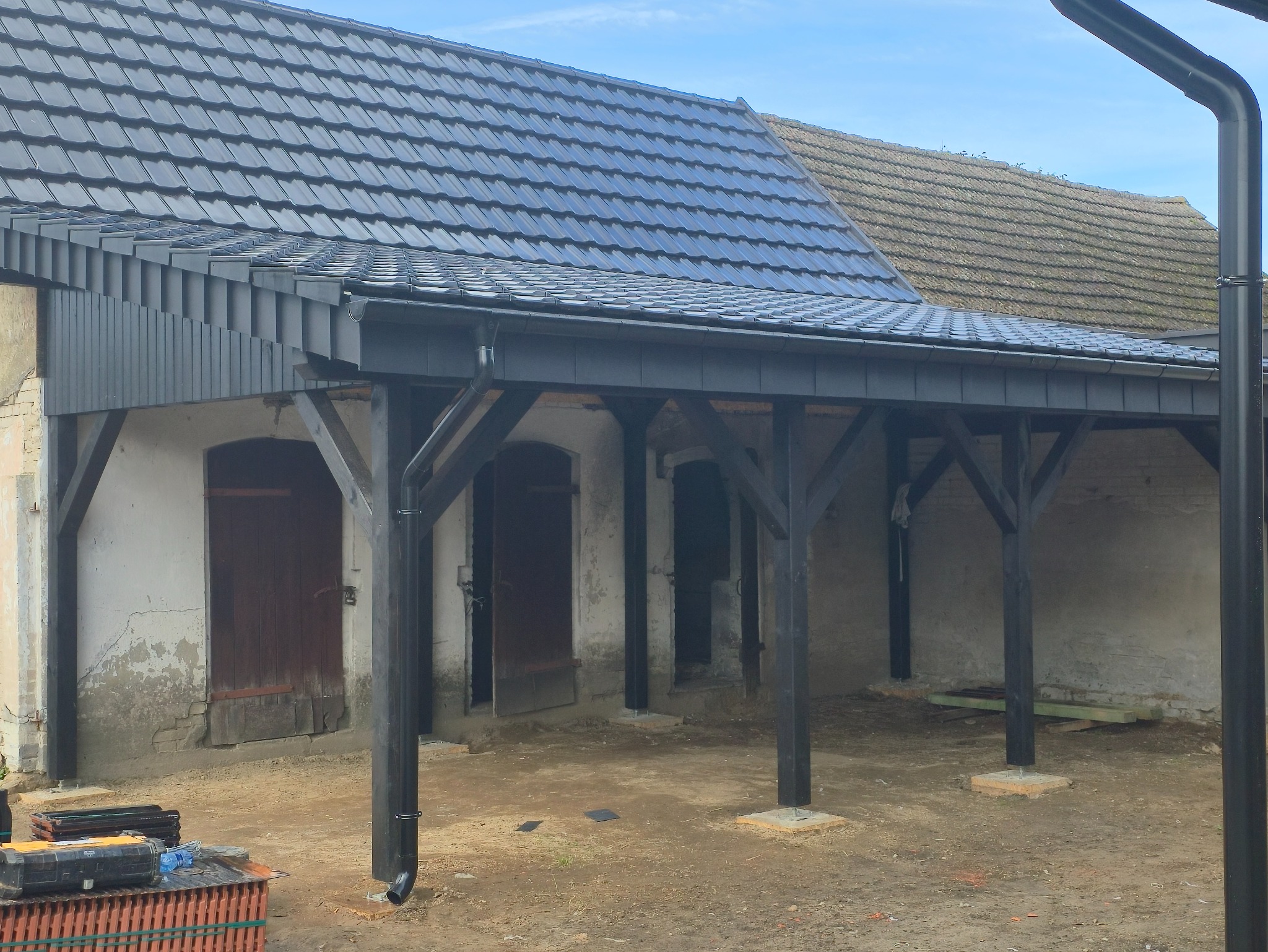 Nowy grafitowy dach z rynnami na drewnianej konstrukcji w stylu rustykalnym. Widoczne narzędzia i materiały budowlane, co sugeruje etap prac wykończeniowych.