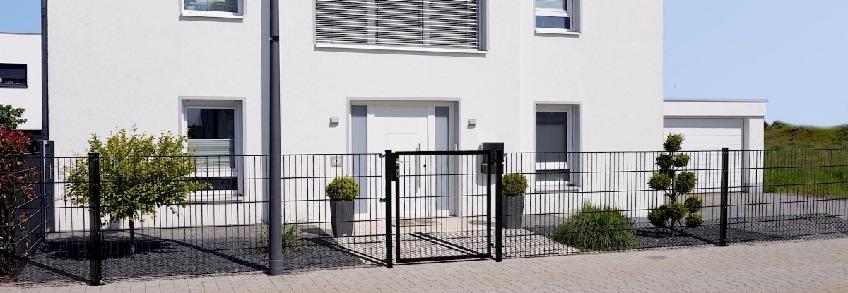 Nowoczesne, czarne ogrodzenie panelowe z furtką i bramą w Ahlen, otaczające biały dom z szarymi elementami dekoracyjnymi i zadbanym ogrodem.