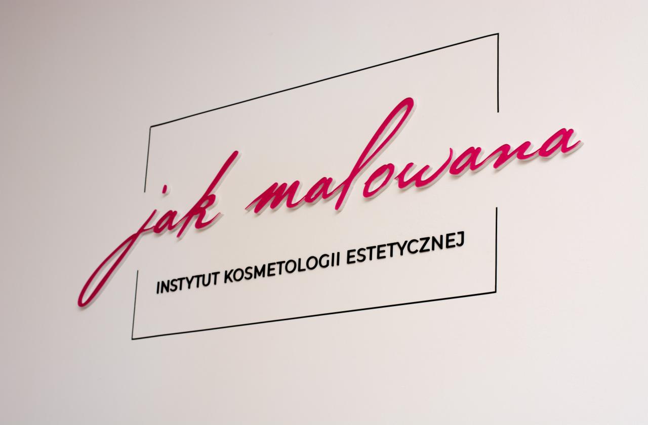 Eleganckie logo 'Jak malowana' Instytutu Kosmetologii Estetycznej na białej ścianie, z różowym, ozdobnym napisem i prostą, czarną ramką.
