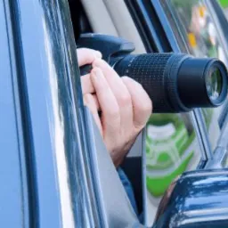 Osoba trzyma aparat fotograficzny z dużym obiektywem, wystawiając go przez okno samochodu.