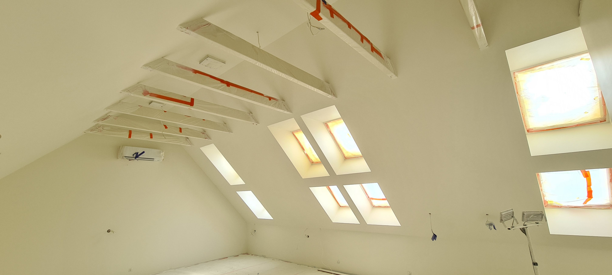 Poddasze po remoncie, ściany pomalowane na jasny odcień, okna dachowe zabezpieczone folią malarską, widoczne elementy konstrukcyjne dachu również zabezpieczone, podłoga częściowo zakryta folią...