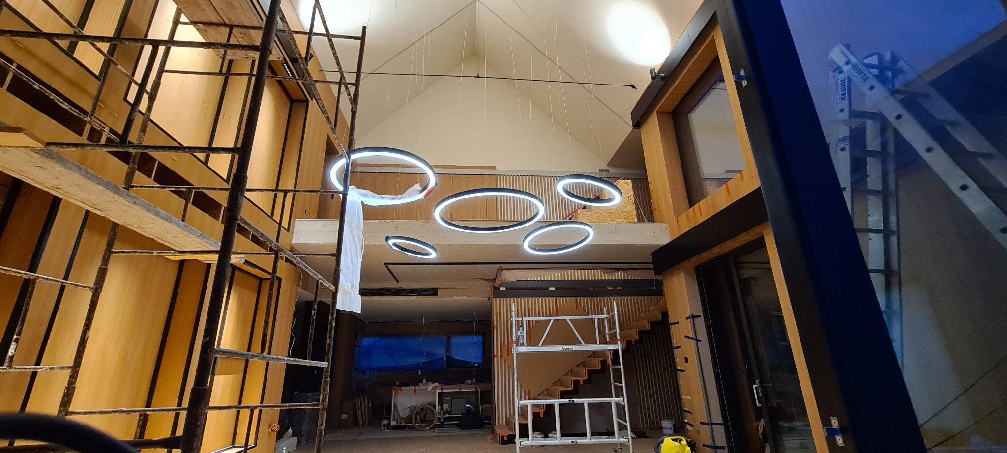 Wnętrze w trakcie remontu w Kamieńcu Wrocławskim: widoczne rusztowania, surowe drewniane ściany, schody w trakcie montażu i nowoczesne, okrągłe lampy sufitowe.