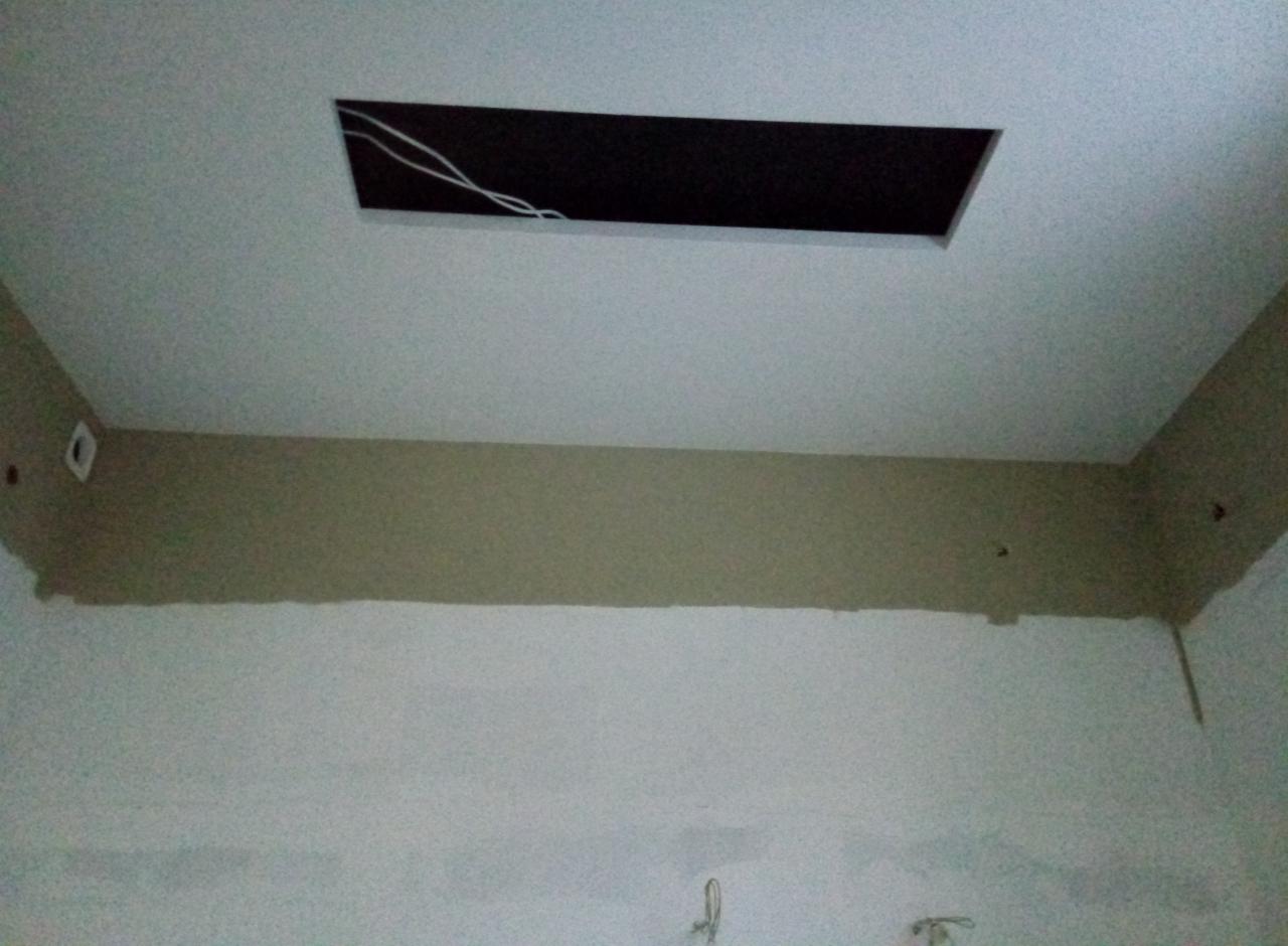 Ściana w trakcie malowania, z widoczną częściowo pomalowaną górną partią w kolorze beżowym i otworem w suficie z wystającymi kablami.