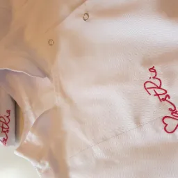 Biała bluza robocza z wyhaftowanym czerwonym napisem 'LaestRia', widoczne złożone bluzy z tym samym napisem w tle.