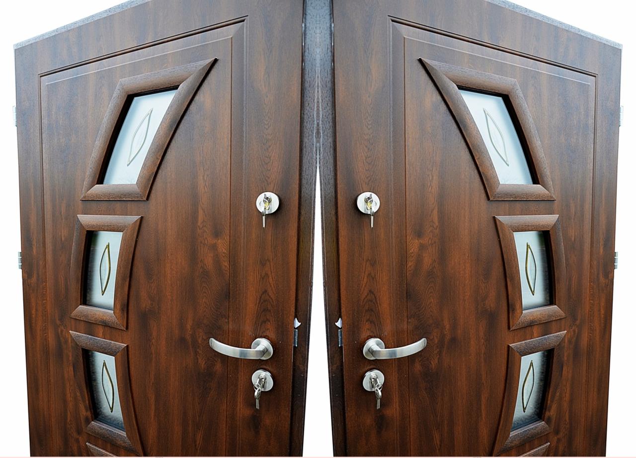 Dwu-skrzydłowe, brązowe drzwi wejściowe z przeszkleniami o geometrycznych kształtach, widoczne klucze w zamkach.