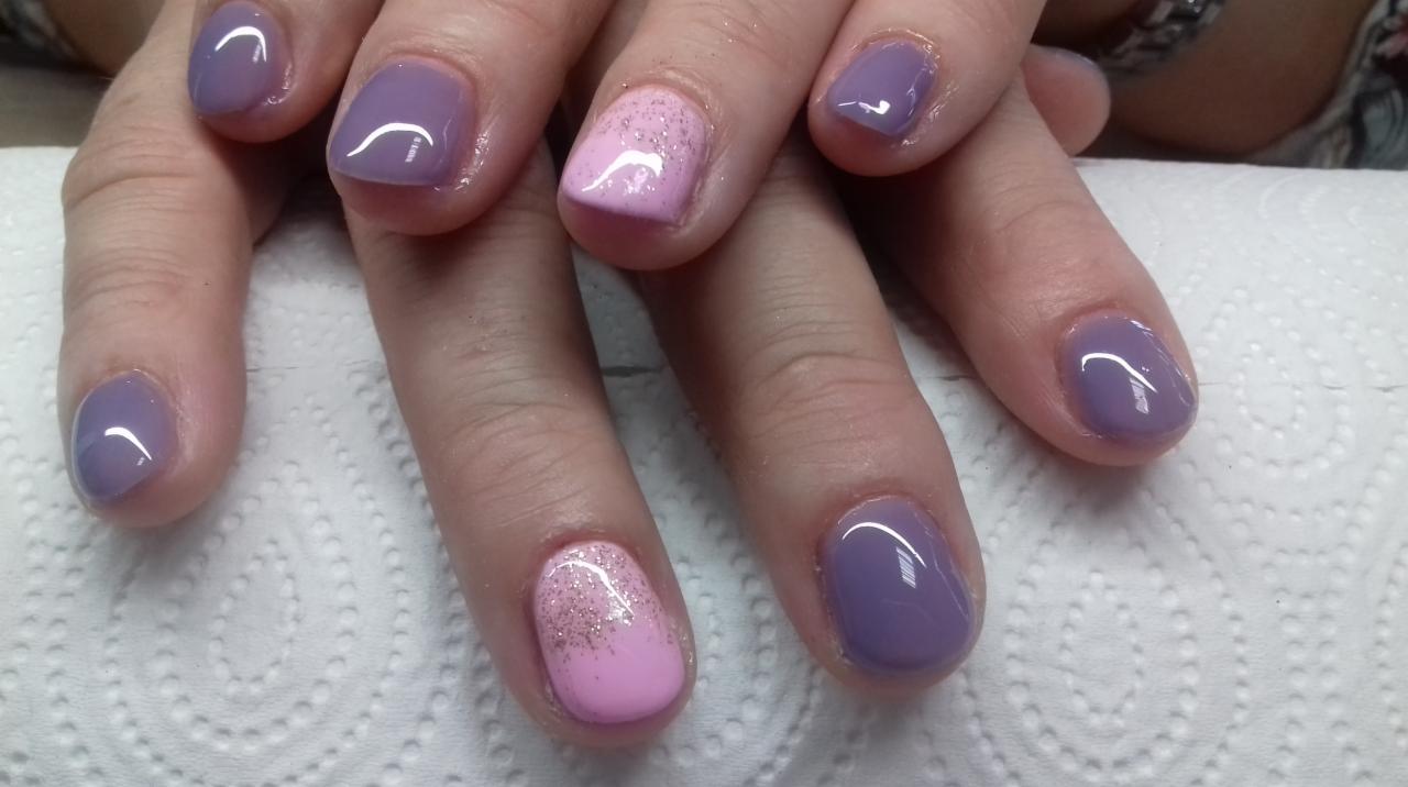 Dłonie z pomalowanymi paznokciami w odcieniach fioletu i różu z brokatem, ułożone na białym ręczniku papierowym.