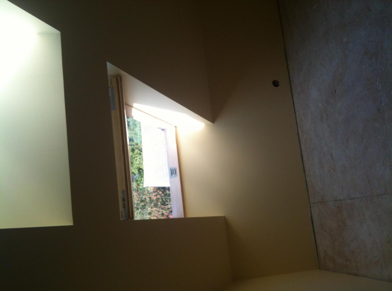 Nietypowe okno trójkątne w ścianie, widok na zieleń z zewnątrz, ściana przygotowana do malowania, widoczna płyta OSB na ścianie po prawej stronie.