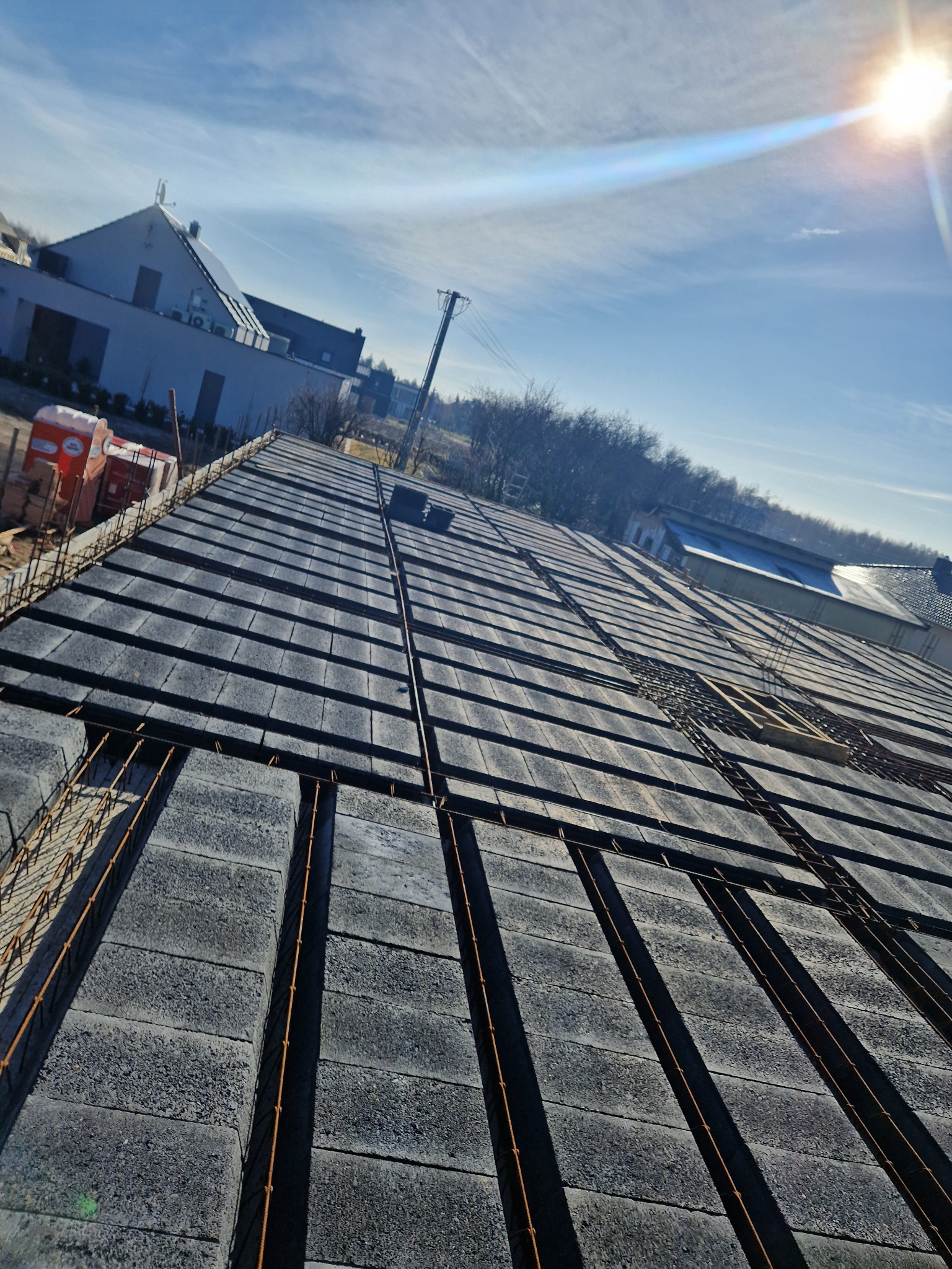 Wiązanie zbrojenia na stropie z szarych bloczków betonowych, widok z góry na budowę domu jednorodzinnego w słoneczny dzień.