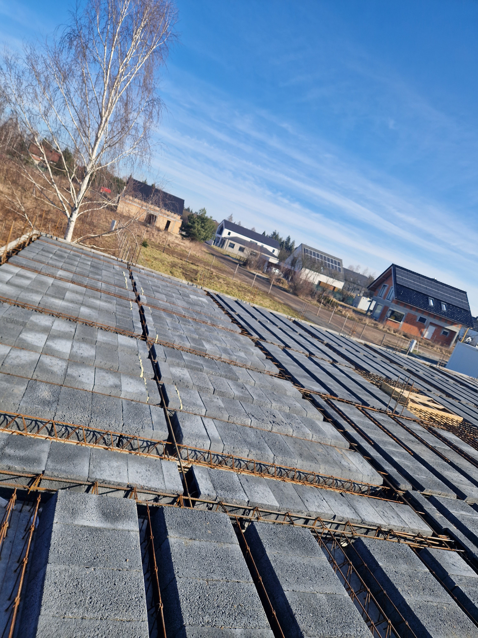 Wykonywanie stropu Teriva z pustaków szarych betonowych i zbrojenia stalowego, widok z góry na budowę domu jednorodzinnego w słoneczny dzień.