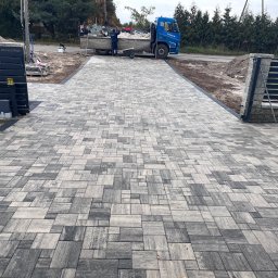 AS.PROJEKT Szymon Majewski - Nowo ułożona, szara kostka brukowa na podjeździe, z widocznym fragmentem bramy i samochodem dostawczym w tle.