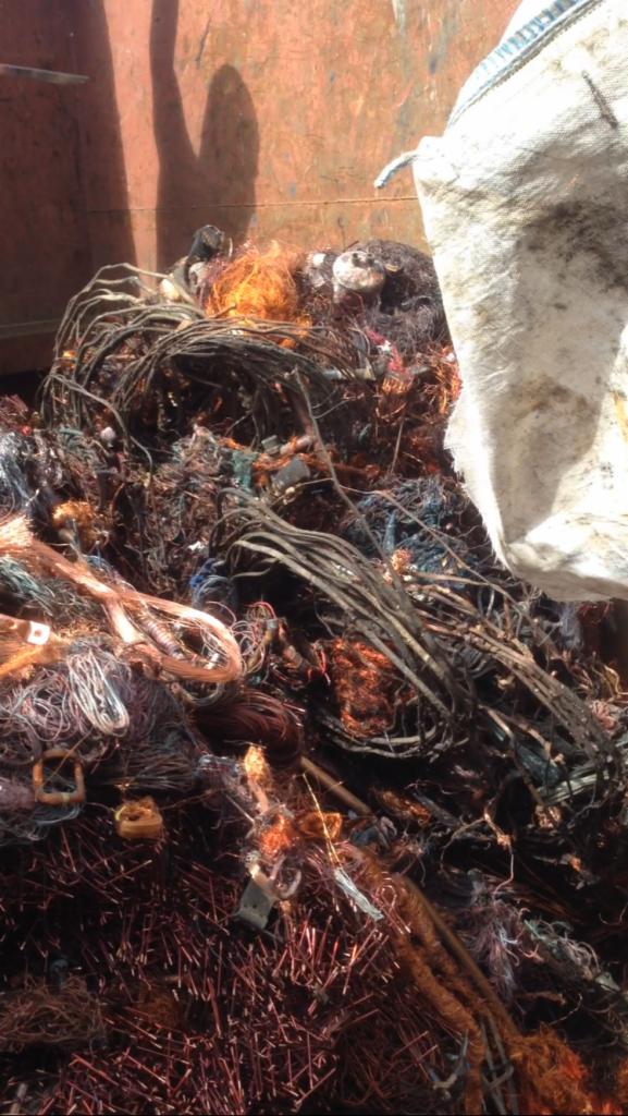 Kupa posegregowanego złomu miedzianego i kabli w kontenerze, przygotowana do transportu, z widocznym workiem na górze.