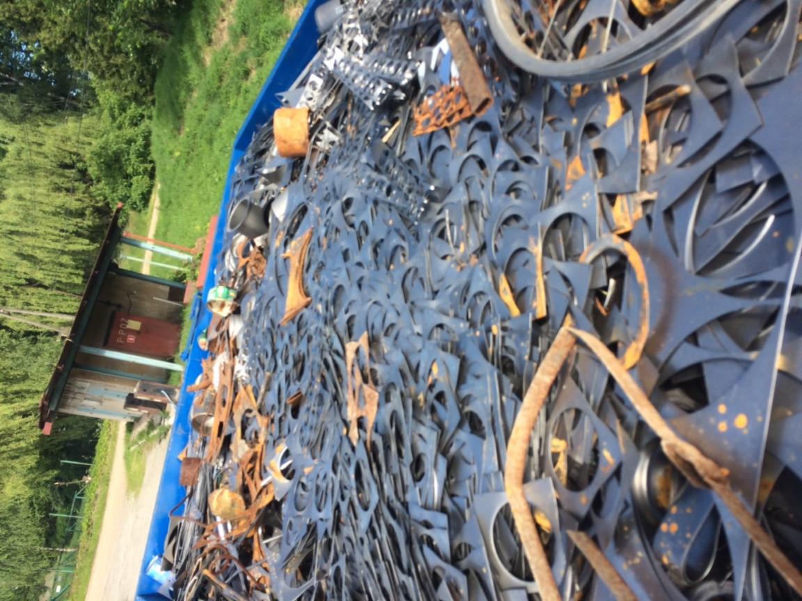 Kontener wypełniony metalowymi odpadami po cięciu laserowym, widoczne rdzewiejące elementy i opona rowerowa na wierzchu.