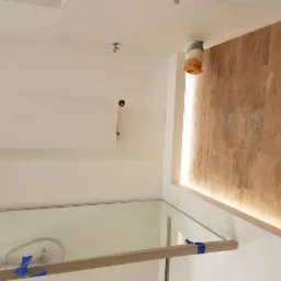 Montaż kabiny prysznicowej z drewnopodobnymi płytkami ściennymi i podświetleniem LED, rury zabezpieczone pomarańczową folią.