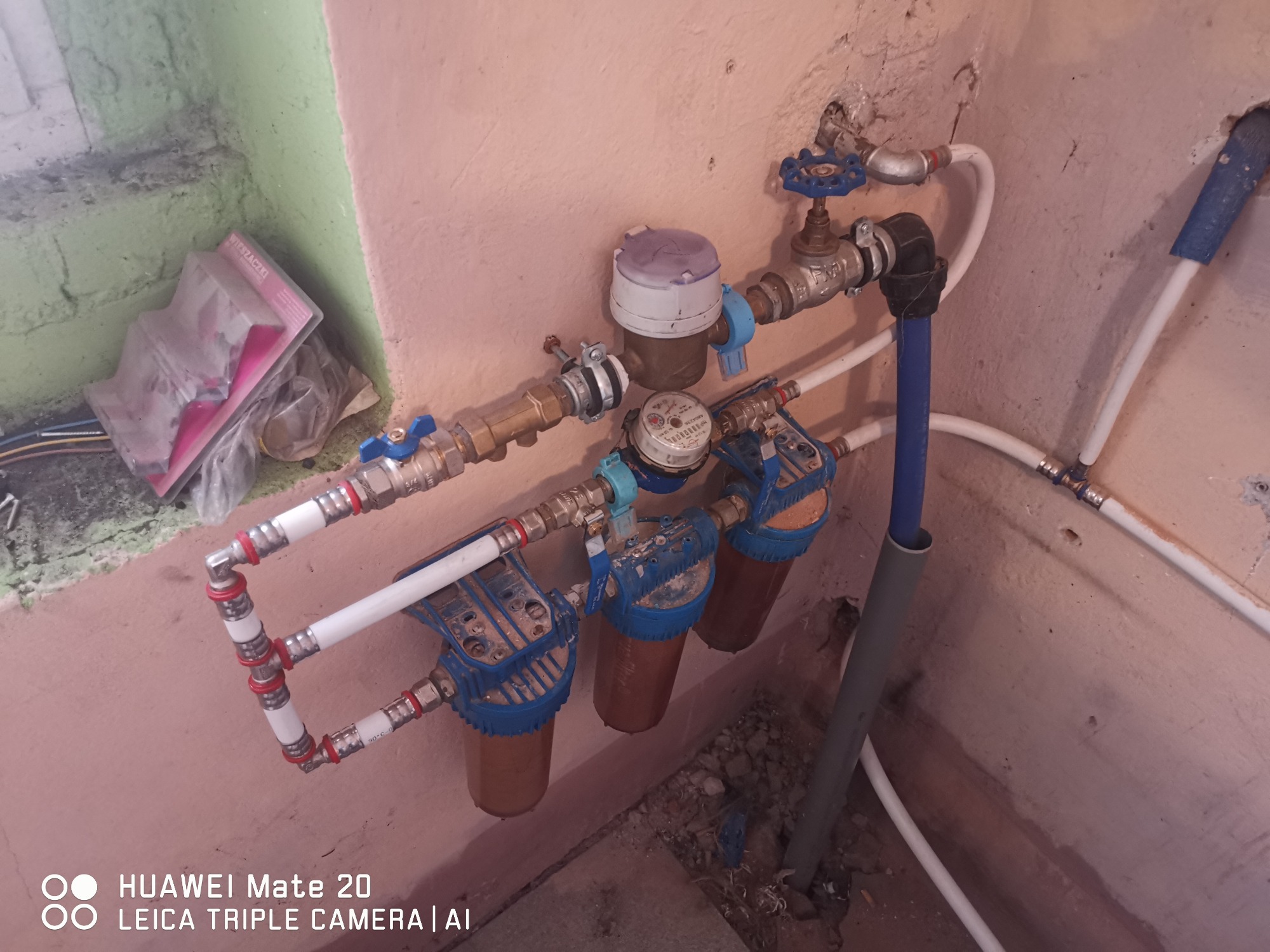 Zamontowane filtry wody z licznikiem, widoczne złącza z zaworami i rurami w pomieszczeniu z surowymi ścianami.