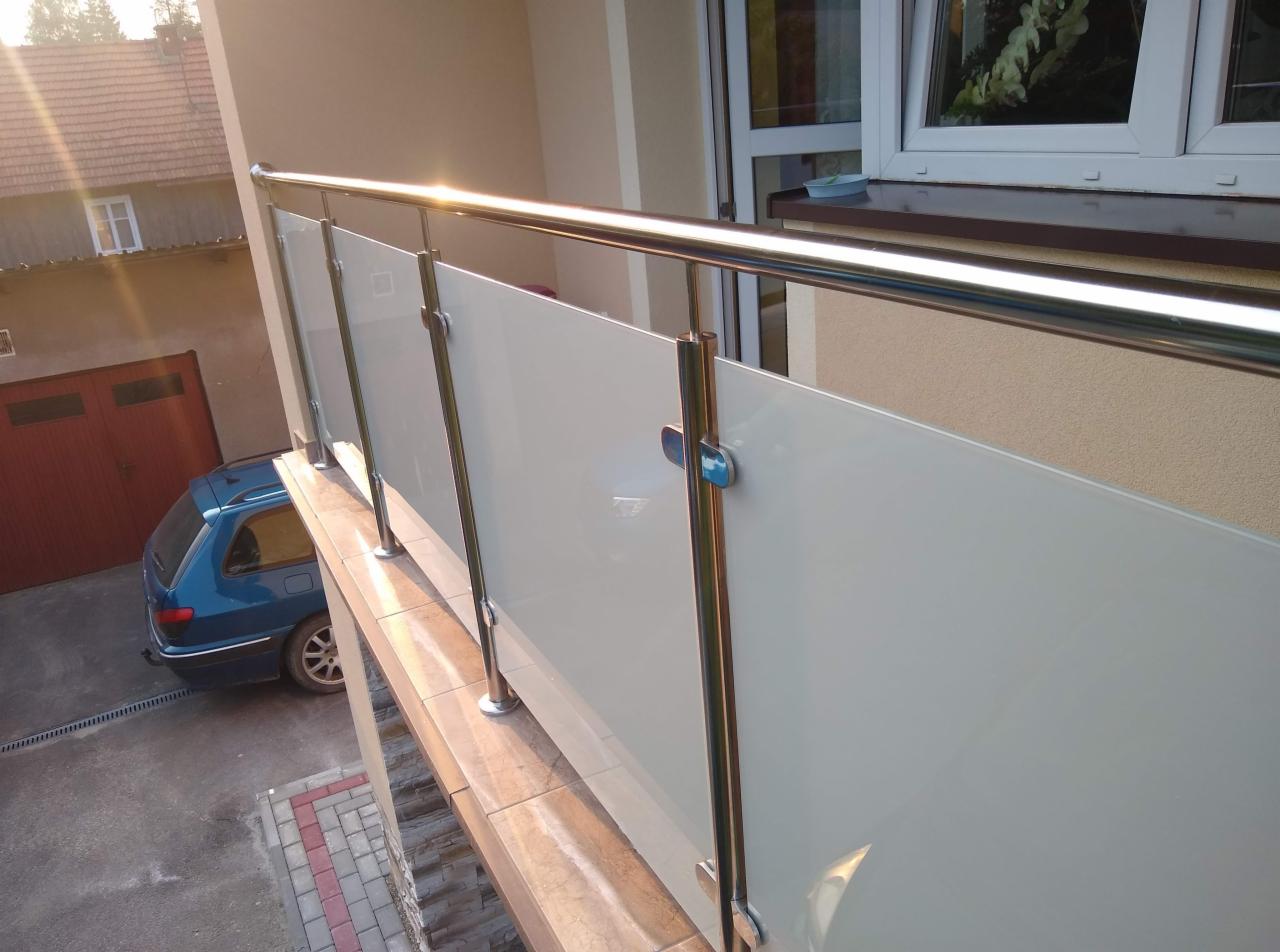 Barierka balkonowa z mlecznego szkła i polerowanej stali nierdzewnej, widoczna z góry, z odbiciem słońca na poręczy, z zaparkowanym niebieskim kombi w tle.