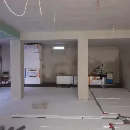 Wnętrze w trakcie ocieplania: podłoga pokryta białym styropianem, widoczne paczki styropianu Izołbet przy ścianie, przygotowane do dalszych prac izolacyjnych.