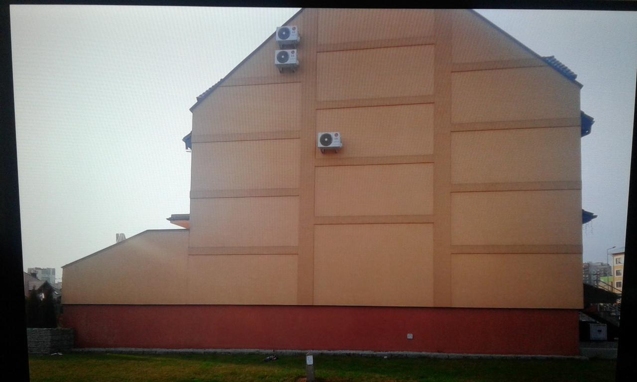 Elewacja budynku wielorodzinnego z trzema klimatyzatorami zamontowanymi na ścianie, widok z poziomu trawnika.