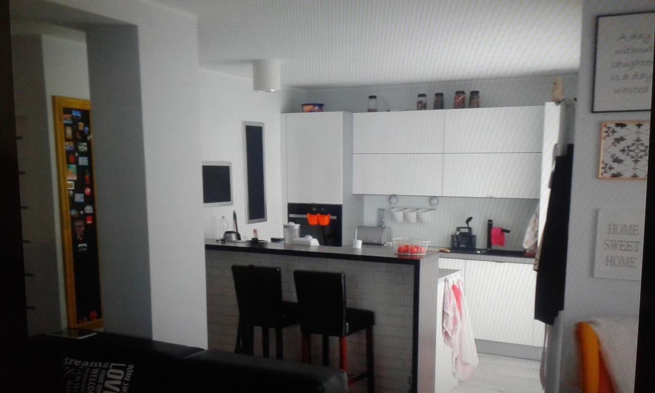 Nowoczesna, jasna kuchnia z białymi szafkami, czarnym blatem i hokerami, minimalistyczny design, dekoracje ścienne.