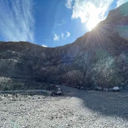 Widok wnętrza kamieniołomu z wyraźnymi warstwami skalnymi, oświetlonego promieniami słonecznymi przebijającymi się przez chmury na błękitnym niebie.