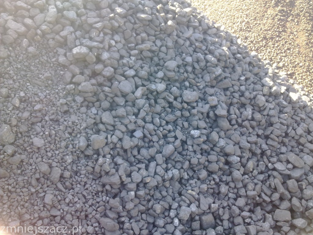 Kupa miału węglowego z widocznymi bryłkami węgla, oświetlona z prawej strony, z widoczną strukturą podłoża.