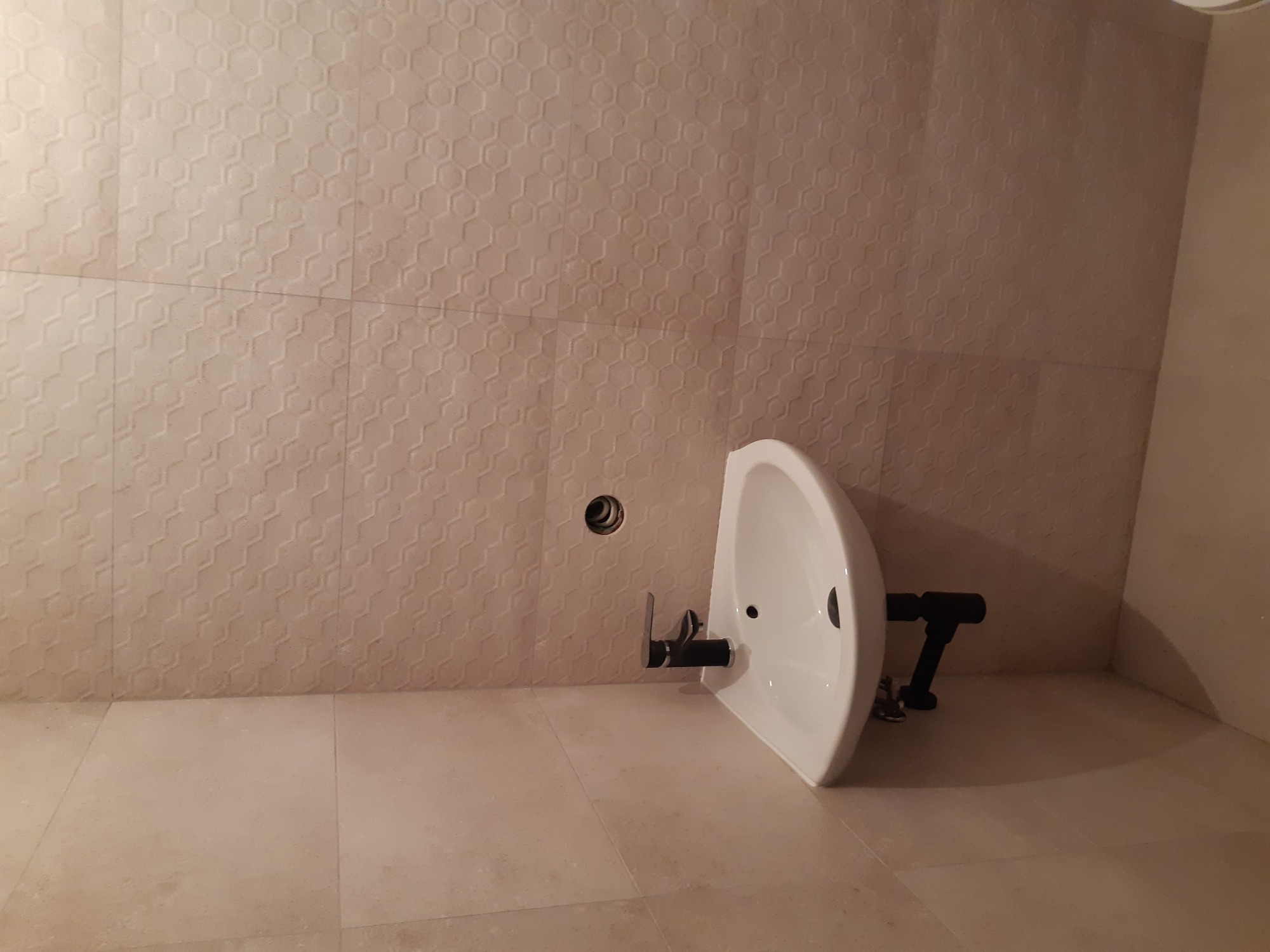 Montaż wiszącej umywalki z czarną armaturą na ścianie z beżowych płytek o wzorze plastra miodu w łazience.