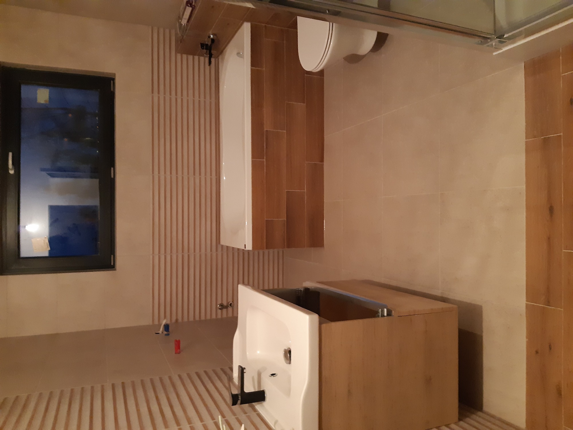 Nowoczesna łazienka z beżowymi płytkami, wiszącą toaletą, umywalką z szafką z drewnopodobnego materiału i pionowymi dekoracyjnymi panelami ściennymi.