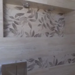 Beżowe płytki z motywem liści w łazience, wnęka z oświetleniem i przycisk spłuczki