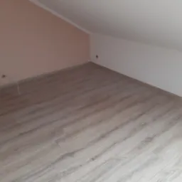 Poddasze z nowo ułożonymi panelami podłogowymi w odcieniach szarości, ściany pomalowane w górnej części na biało, w dolnej na pudrowy róż.