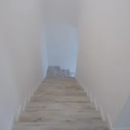 Schody wewnętrzne wyłożone panelami imitującymi drewno, białe ściany i listwy przypodłogowe, widok z góry w dół.