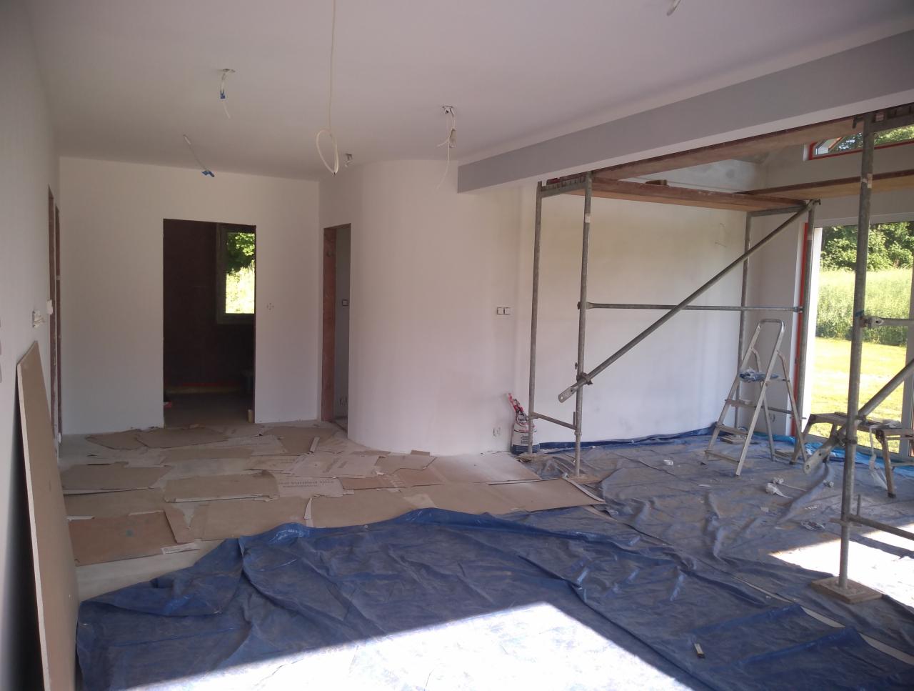 Wnętrze w trakcie prac: świeżo pomalowane białe ściany, zabezpieczona folią podłoga, rozstawione rusztowanie, widoczne kable instalacji elektrycznej, surowy stan wykończenia.