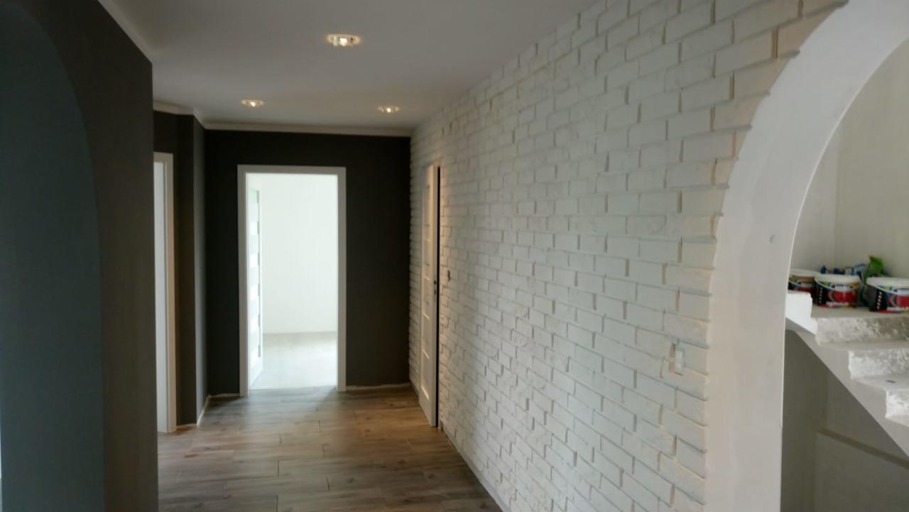 Korytarz po remoncie w Górce Prudnickiej z białą ceglaną ścianą, ciemnoszarymi ścianami, drewnopodobną podłogą i białymi drzwiami.