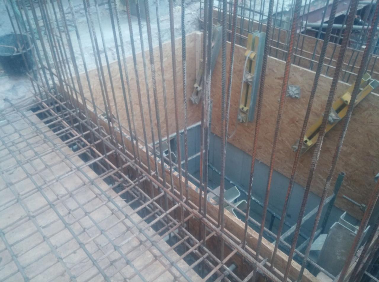 Zbrojenie fundamentów z szalunkiem z desek i poziomnicami. Widoczne pręty zbrojeniowe i siatka, przygotowane do zalania betonem. Ujęcie z góry, bliski plan.