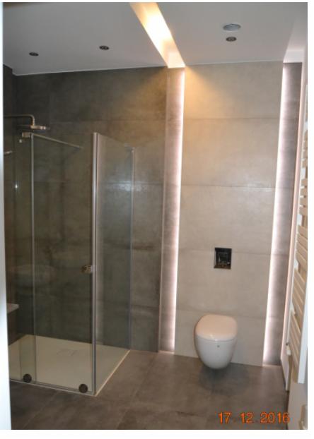 Nowoczesna łazienka z kabiną prysznicową typu walk-in, podświetlanymi pionowymi panelami ściennymi LED, wiszącą toaletą i szarą płytką podłogową.