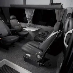 Wnętrze luksusowo wyposażonego busa do przewozu osób z regulowanymi fotelami, rozkładanym stolikiem i zasłonami w oknach.