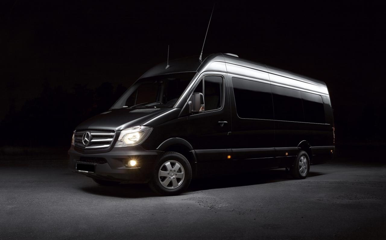 Czarny Mercedes-Benz Sprinter z przyciemnianymi szybami, oświetlony reflektorami na ciemnym tle.