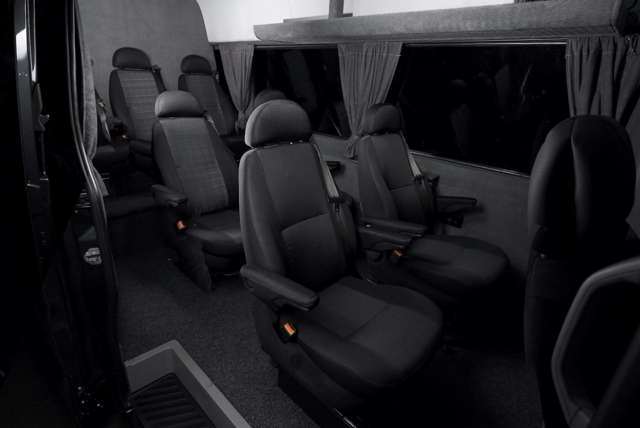 Wnętrze luksusowego busa z ciemnymi, skórzanymi fotelami z podłokietnikami i zasłonami w oknach.