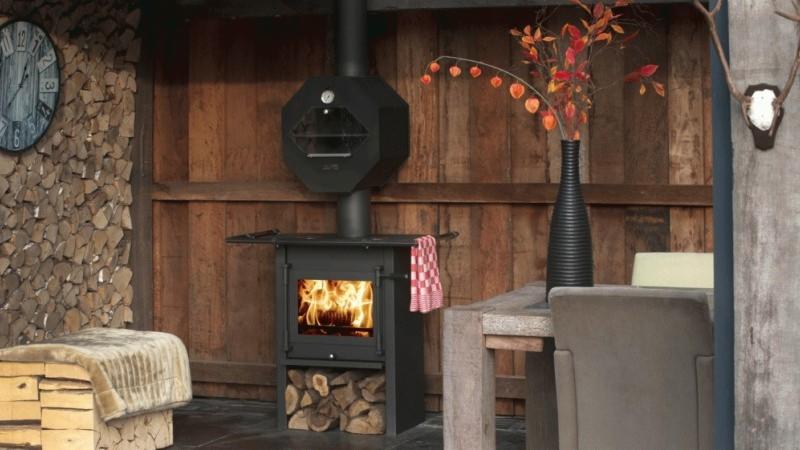 Czarny piec na paliwo stałe z paleniskiem, płomieniami i zapasem drewna, ustawiony w rustykalnym wnętrzu z drewnianymi ścianami i dekoracjami.