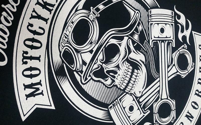 Czarno-biały nadruk na koszulce z motywem motocyklowym: czaszka w goglach i kask retro, skrzyżowane tłoki silnika, napis 'Motocykle Hardcore'.