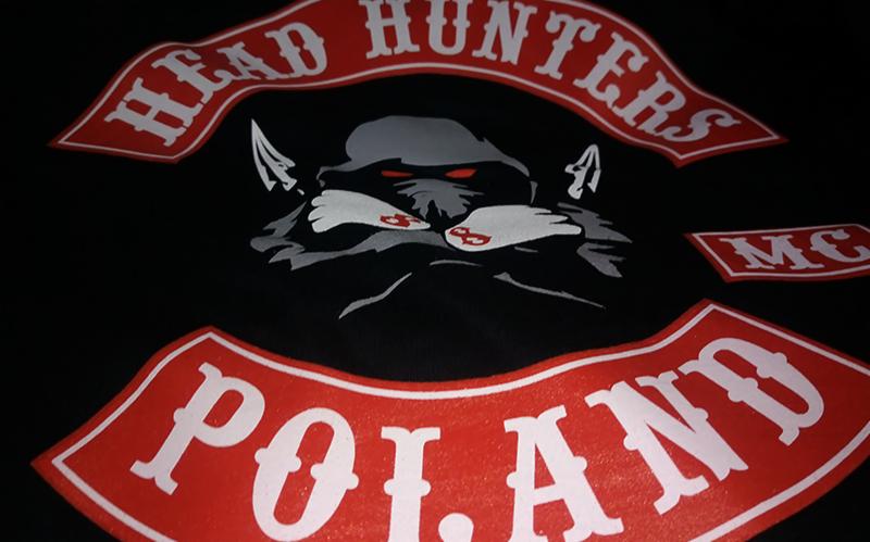 Czarna koszulka z nadrukiem motywu motocyklowego klubu Head Hunters Poland MC, z dominującym szarym wilkiem o czerwonych oczach i napisami w czerwonych obramowaniach.