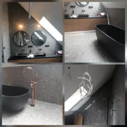 Nowoczesna łazienka na poddaszu z czarną wanną wolnostojącą, grafitową mozaiką i elementami miedzianymi. Widoczne okno dachowe i minimalistyczne umywalki.