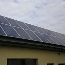 Panele słoneczne na dachu budynku jednorodzinnego, widok z dołu, pochmurne niebo w tle.