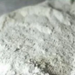 Biały, sypki proszek o nierównej strukturze, przypominający wapno lub produkt mineralny, sfotografowany z bliska.