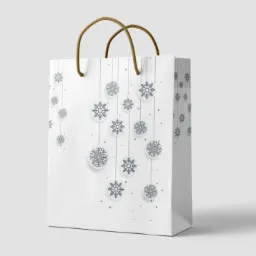 Biała torba prezentowa z motywem płatków śniegu i sznurkowymi uchwytami, ustawiona na jasnym tle.