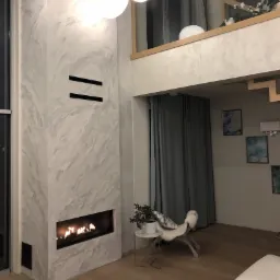 Dwupoziomowy salon z kominkiem w obudowie z efektem trawertynu, oświetlony trzema kulistymi lampami wiszącymi, z widoczną antresolą i elementami dekoracyjnymi.