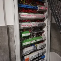 Otwarta szafa sterownicza z licznymi modułami elektronicznymi Nexwell, przewodami w różnych kolorach, listwami zaciskowymi i elementami zabezpieczającymi.