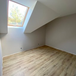 Mal-Pol - Poddasze z oknem dachowym i panelami podłogowymi w odcieniach beżu, świeżo po malowaniu ścian na jasny kolor, widoczne gniazdko elektryczne.