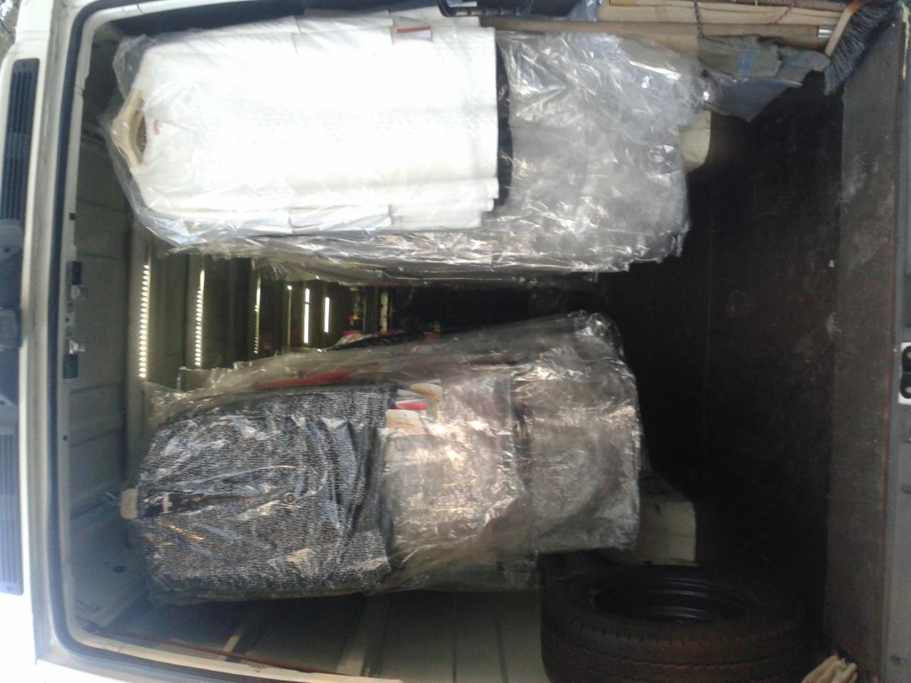 Wnętrze furgonetki załadowane dwoma spakowanymi materacami i oponą, widoczne zabezpieczenia towaru folią.